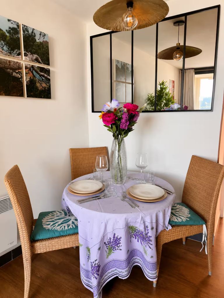 Coin repas de l'appartement avec table ronde dressée, chaises en rotin et grand miroir de style atelier