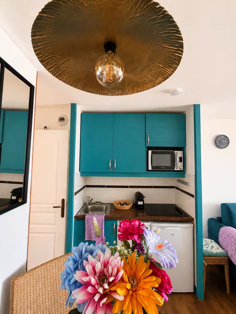 Cuisine équipée aux façades bleu canard avec plaque de cuisson, micro-ondes, réfrigérateur et machine à café