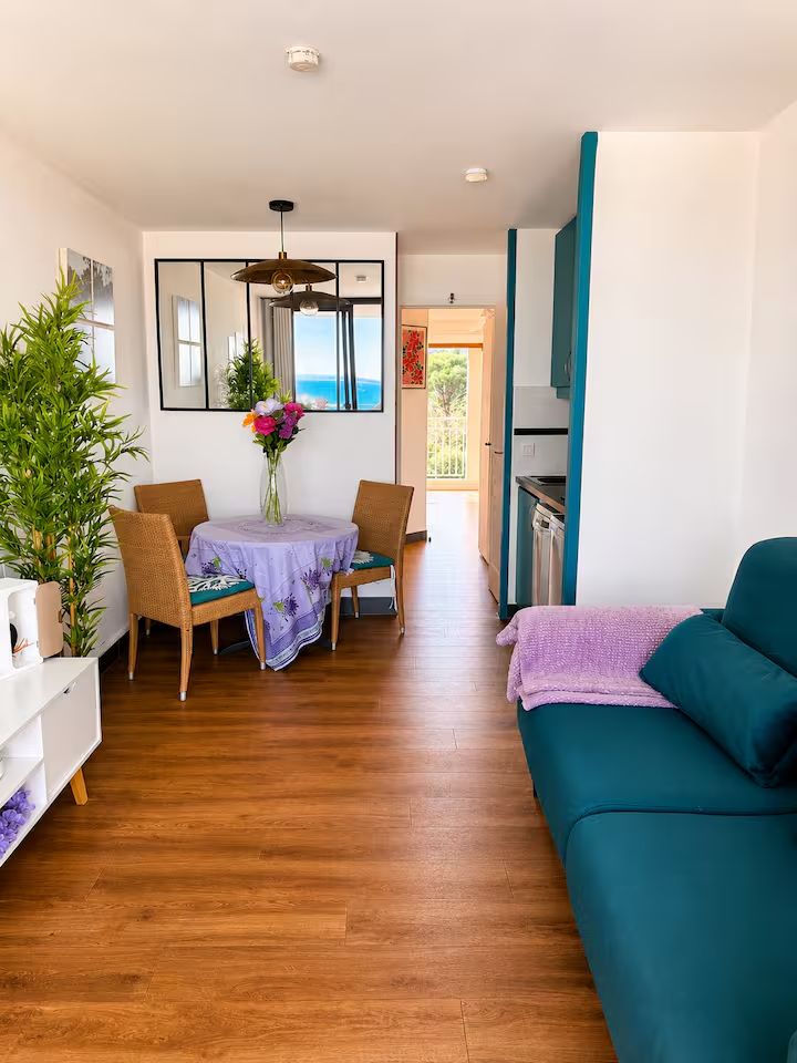 Séjour de l'appartement Blue View Cannes : canapé bleu canard, table ronde et ouverture sur le balcon avec la mer en arrière-plan