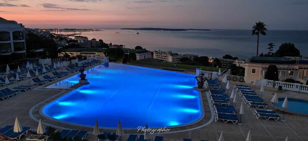 La piscine de la résidence Villa Francia illuminée au crépuscule, avec les lumières de Cannes et la mer à l'horizon