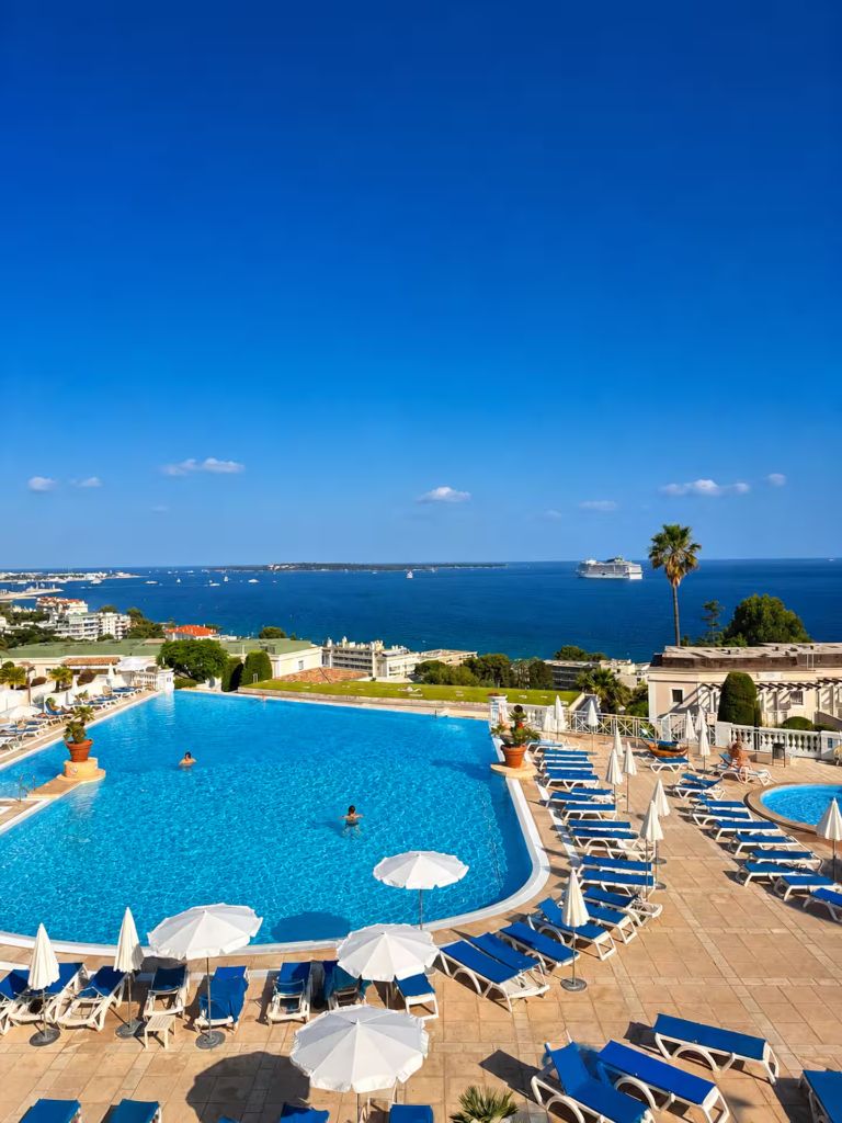 Grande piscine de la résidence Villa Francia bordée de transats bleus, face à la baie de Cannes et aux îles de Lérins